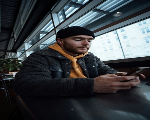 A person sitting at a cafe table looking at a mobile phone with poor posture